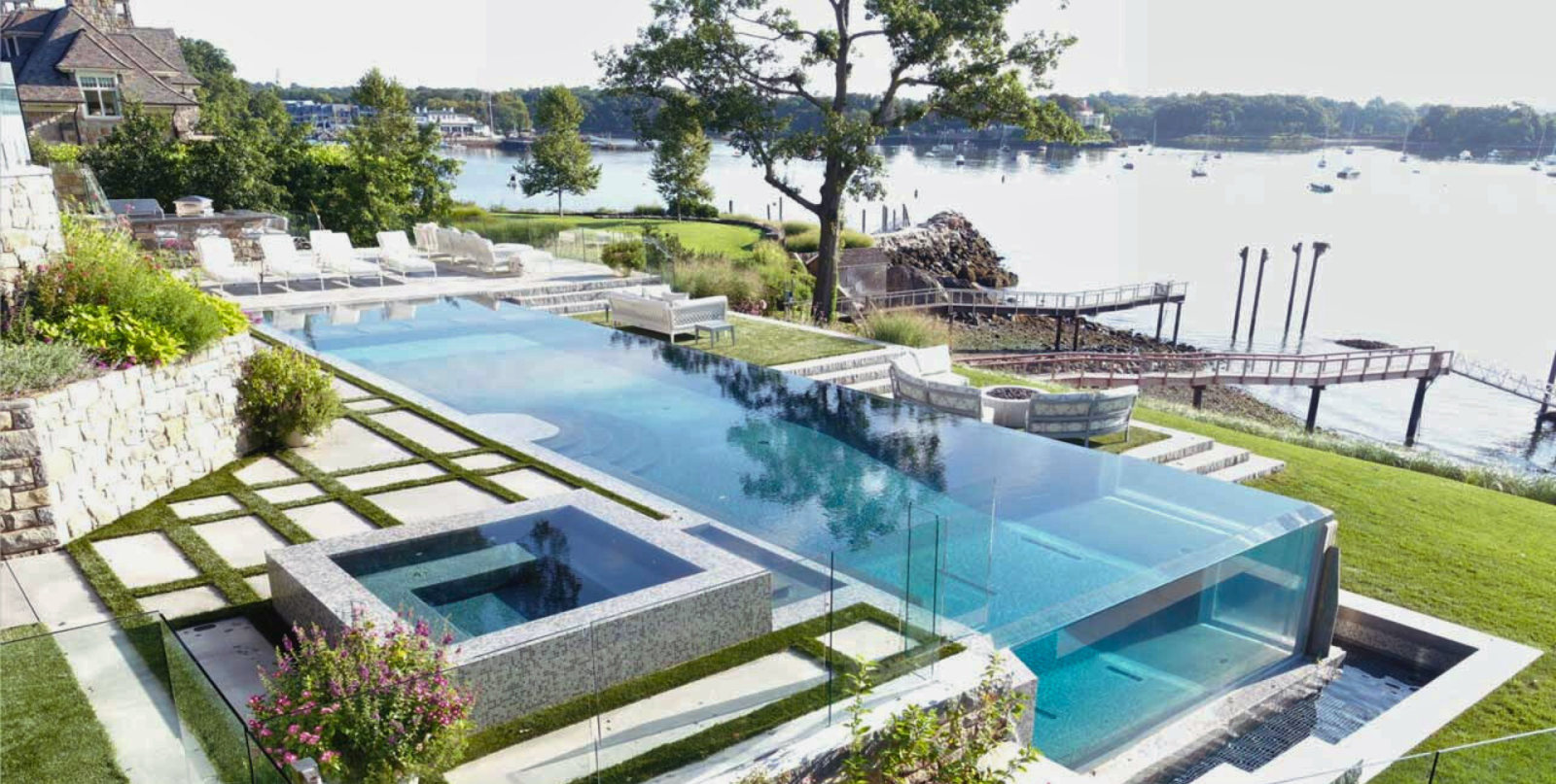 Aerial view of waterfront infinity pool with acrylic window wall overlooking harbor